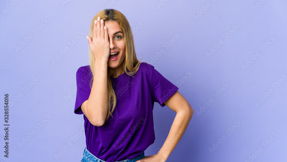 Young blonde woman isolated on purple background having fun covering half of face with palm. Young blonde woman isolated on purple background having fun covering half of face with palm.