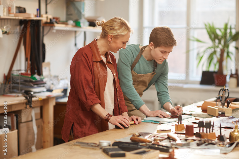 Horizontal shot of young man and cheerful woman working together in modern leather craft shop Horizontal shot of young man and cheerful woman working together in modern leather craft shop