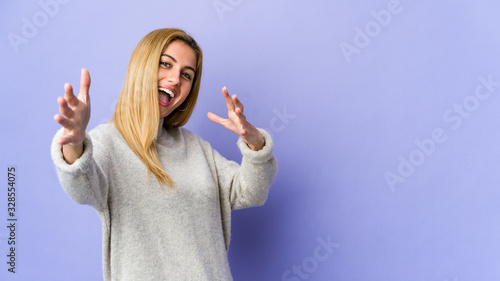Young blonde woman isolated on purple background feels confident giving a hug to the camera.