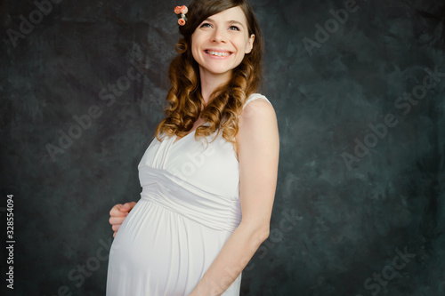 Happy pregnant caucasian young woman on dark backdrop. Maternity, femininity, mother's day concept.