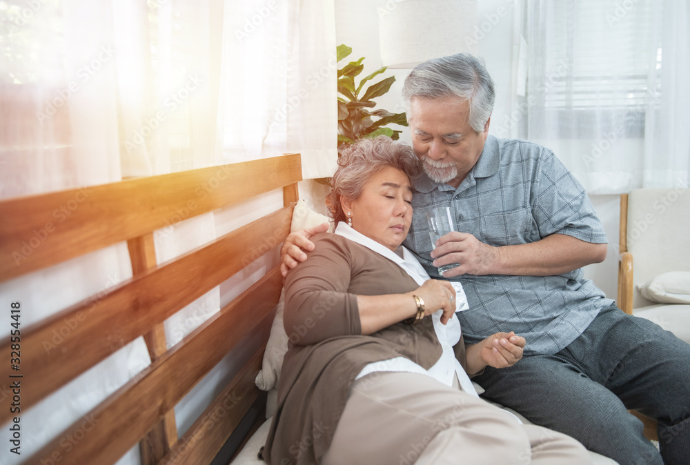 Asian Senior Woman taking medicines and drinking water while sitting on couch. Old man take care his wife while her illness at the house.healthcare and medicine concept.