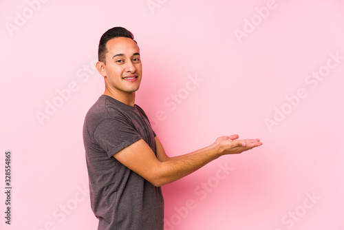 Yooung latin man posing in a pink backgroundholding a copy space on a palm. photo