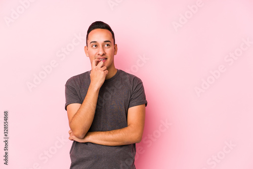 Yooung latin man posing in a pink backgroundrelaxed thinking about something looking at a copy space.