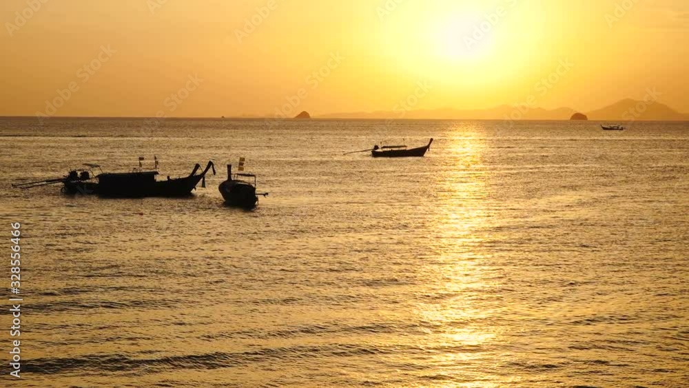 Silhouette of long tail boats with on calm sea surface at sunset with yellow blue sky reflecting on bay of Thailand Silhouette of long tail boats with on calm sea surface at sunset with yellow blue sky reflecting on bay of Thailand