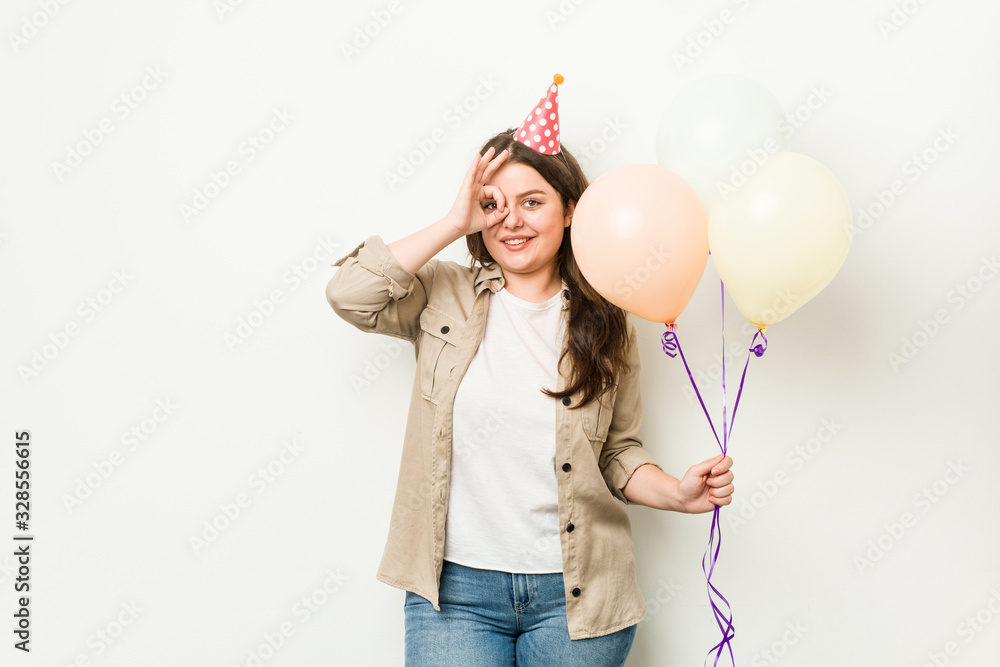 Young plus size curvy woman celebrating a birthday excited keeping ok gesture on eye. Young plus size curvy woman celebrating a birthday excited keeping ok gesture on eye.