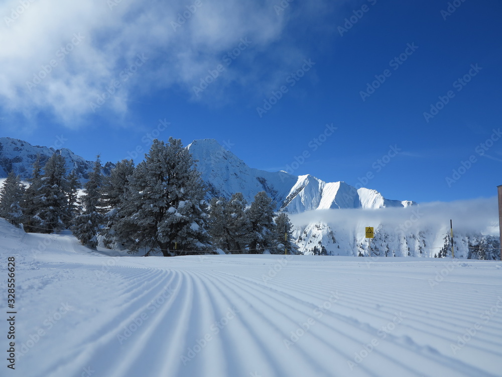 Snow velvet close up on ski slope on the background of snowy mountain peaks. Prepared ski and snowboard track.