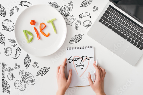 Top view of woman holding pen and notebook with start diet today words near lettering diet from vegetable slices on plate and laptop on white background with vegetables and leaves illustration