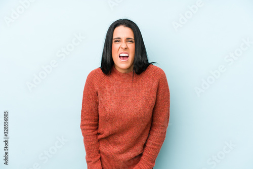 Young caucasian woman isolated on a blue background screaming very angry and aggressive. © Asier