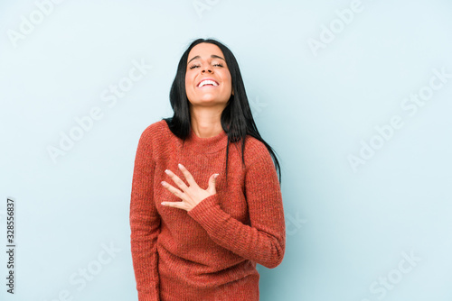 Young caucasian woman isolated on a blue background laughs out loudly keeping hand on chest. © Asier