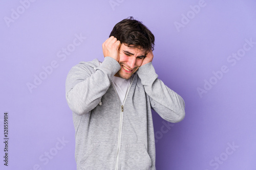 Young man isolated on purple background covering ears with hands.