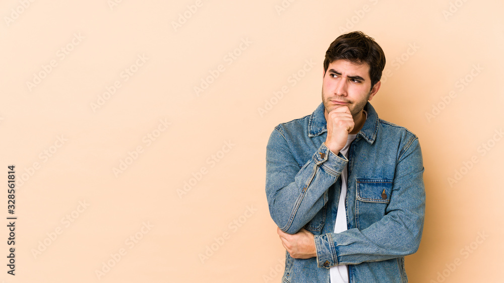 Young man isolated on beige background looking sideways with doubtful and skeptical expression. Young man isolated on beige background looking sideways with doubtful and skeptical expression.