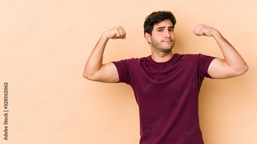 Young man isolated on beige background showing strength gesture with arms, symbol of feminine power Young man isolated on beige background showing strength gesture with arms, symbol of feminine power