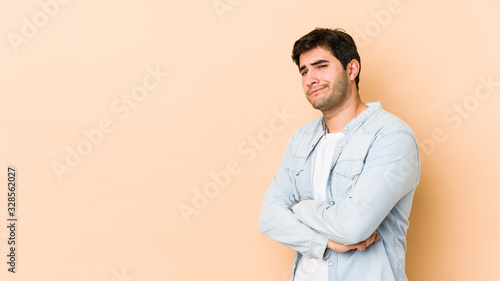 Young man isolated on beige background suspicious, uncertain, examining you.