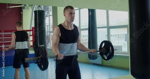 Athletic muscular man doing exercises with a barbell for biceps in a boxing gym. Boxer trains to maintain good physical fitness.