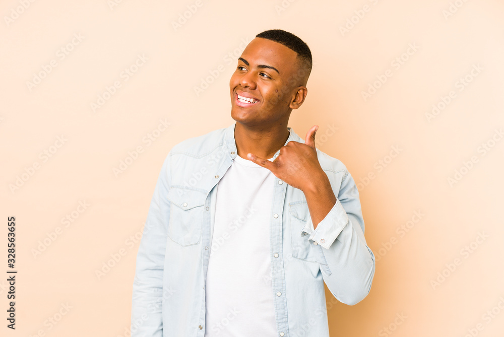 Young latin man isolated on beige background showing a mobile phone call gesture with fingers. Young latin man isolated on beige background showing a mobile phone call gesture with fingers.