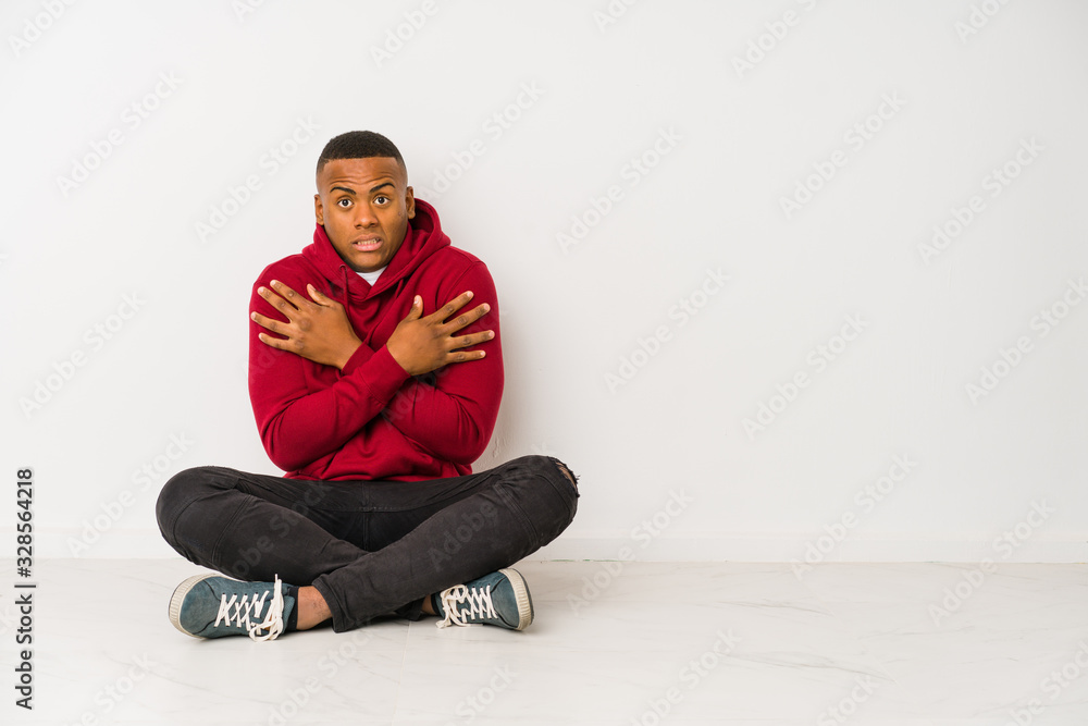 Young latin man sitting on the floor isolated going cold due to low temperature or a sickness. Young latin man sitting on the floor isolated going cold due to low temperature or a sickness.