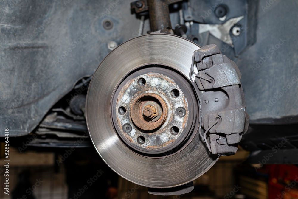 Front brake discs with brake caliper and brake pads in the car, on a car lift in a workshop. Front brake discs with brake caliper and brake pads in the car, on a car lift in a workshop.