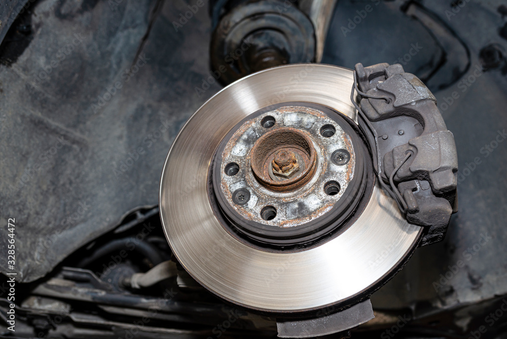 Front brake discs with brake caliper and brake pads in the car, on a car lift in a workshop. Front brake discs with brake caliper and brake pads in the car, on a car lift in a workshop.
