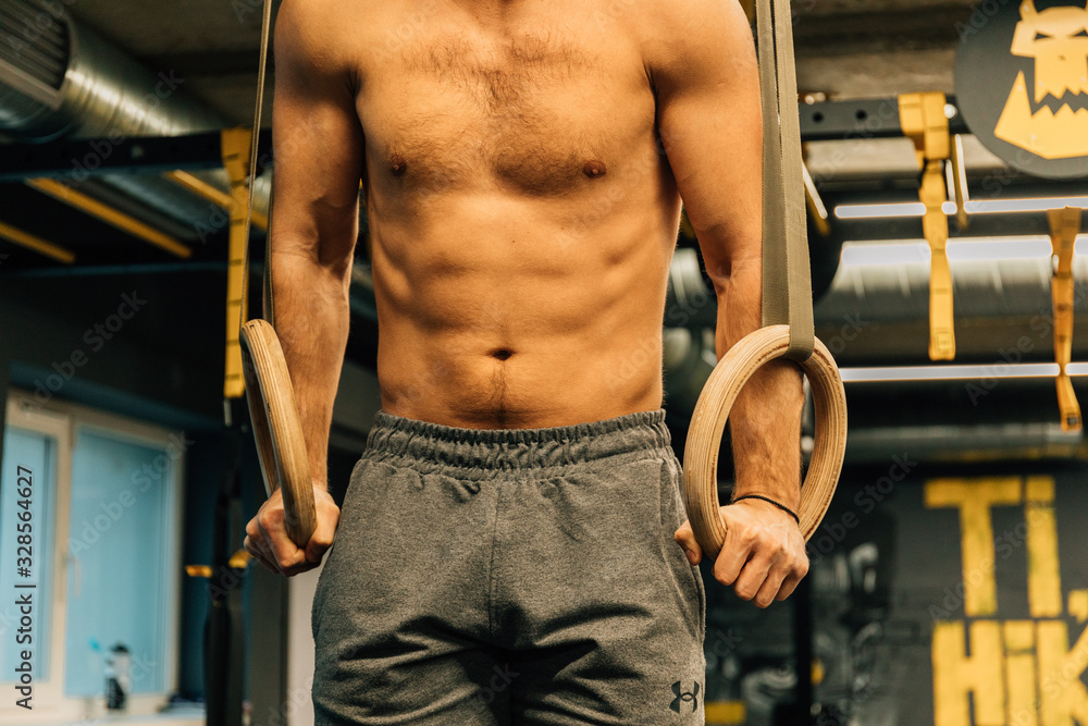 Naklejka premium Muscle up exercise athletic man doing intense workout at the gym on gymnastic rings. Fitness, sport and healthy lifestyle concept.