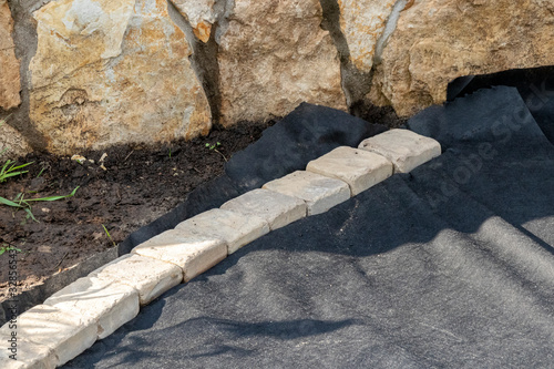 Edging of laid woven geotextile fabric with sandstone pavers in the summer garden under reconstruction