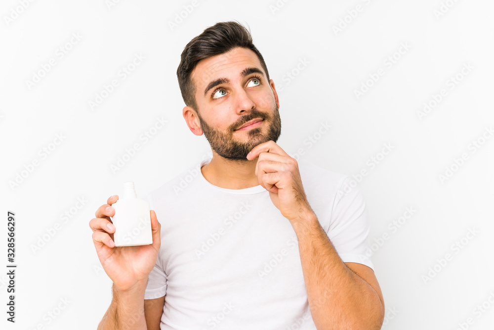 Young caucasian man holding a vitamins bottle isolated looking sideways with doubtful and skeptical expression. Young caucasian man holding a vitamins bottle isolated looking sideways with doubtful and skeptical expression.
