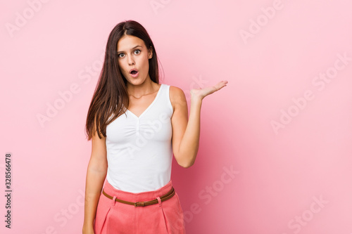 Young cute woman impressed holding copy space on palm.