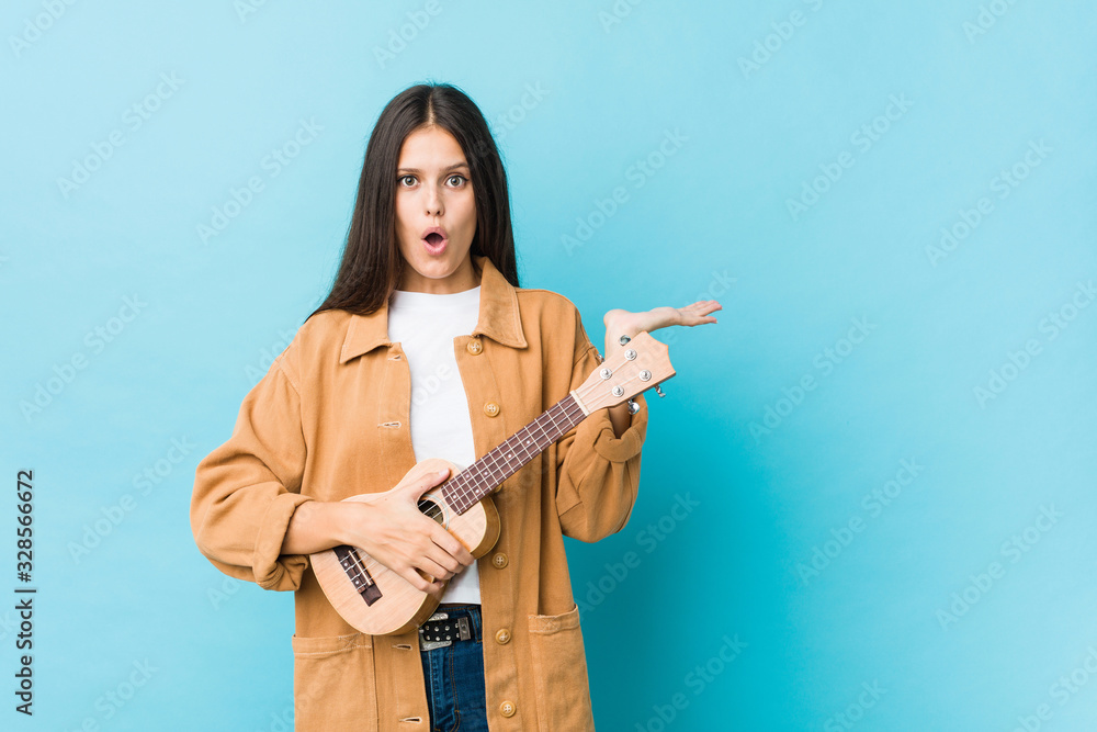 Young caucasian woman holding a ukelele impressed holding copy space on palm. Young caucasian woman holding a ukelele impressed holding copy space on palm.