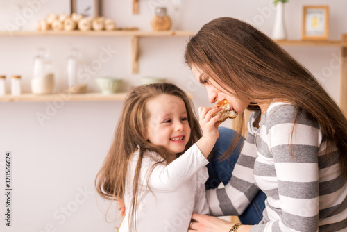 a beautiful little daughter feeds her mother cookies in the kitchen.They eat pancakes and play and laugh