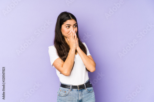 Young indian woman isolated on purple background laughing about something, covering mouth with hands.