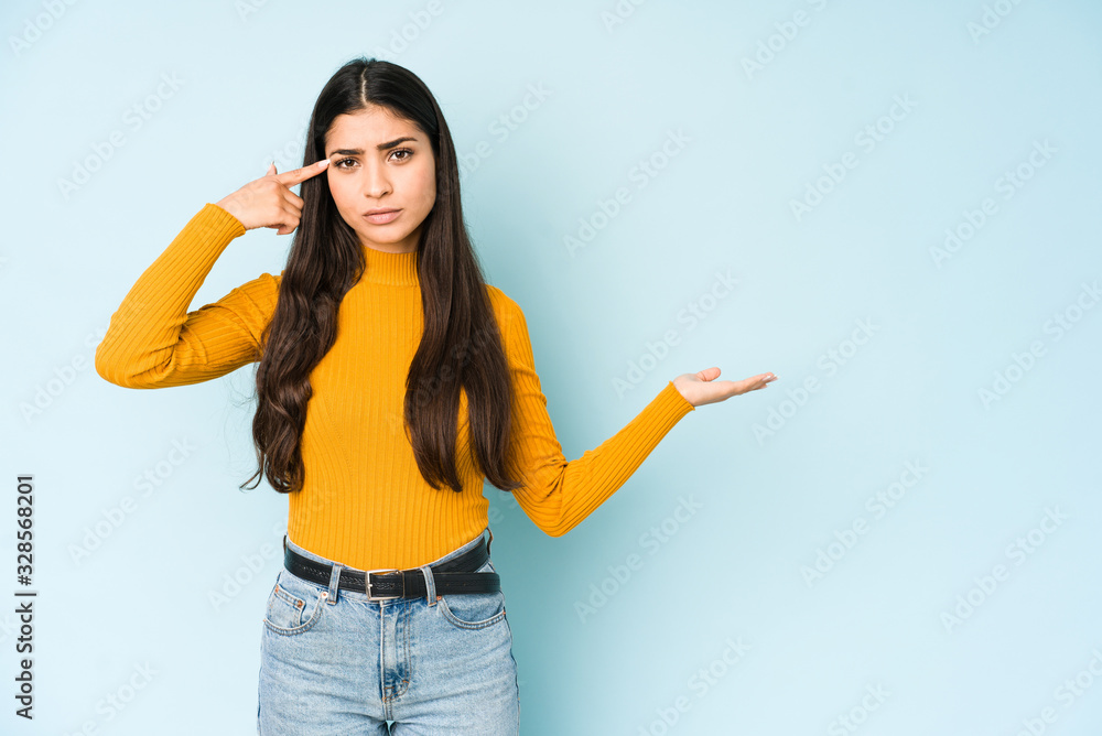 Young indian woman isolated on blue background holding and showing a product on hand. Young indian woman isolated on blue background holding and showing a product on hand.