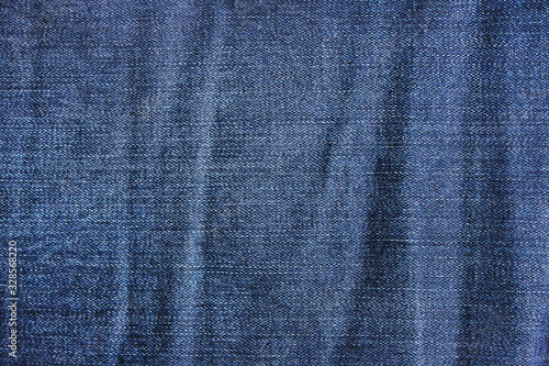 Wrinkled denim jeans cloth, creasy dark blue jean fabric. Worn crumpled jean material, classic clothing detail, creasy jeans close up view