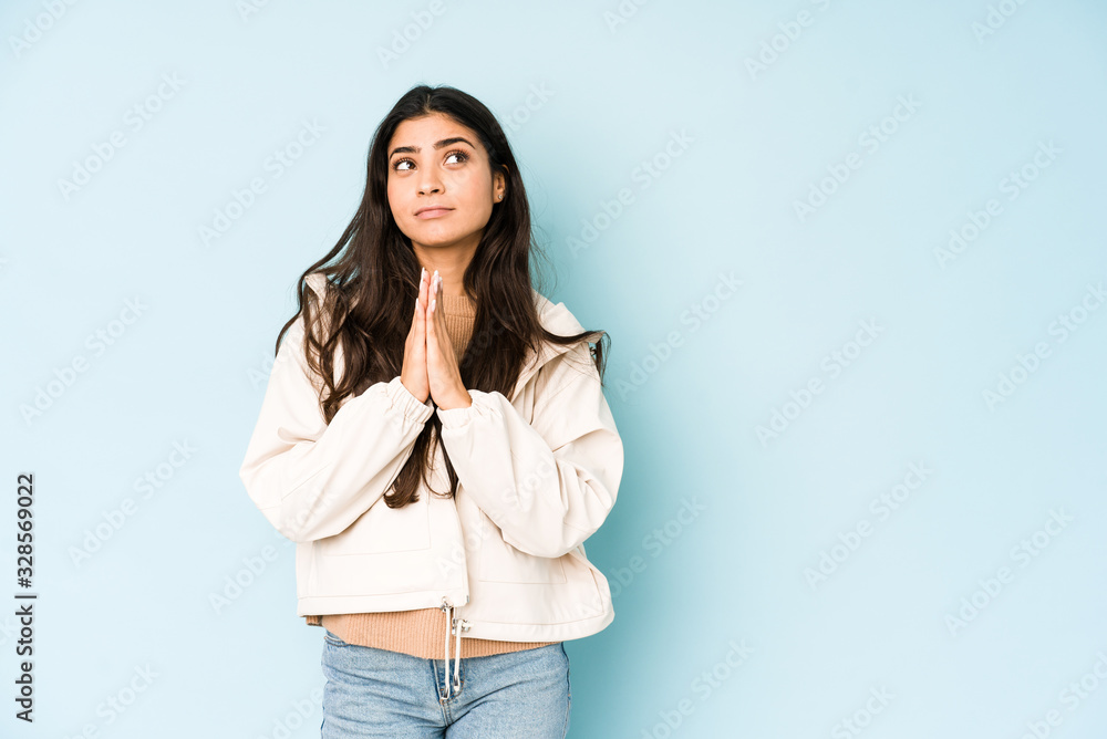 Young indian woman on blue background holding hands in pray near mouth, feels confident. Young indian woman on blue background holding hands in pray near mouth, feels confident.