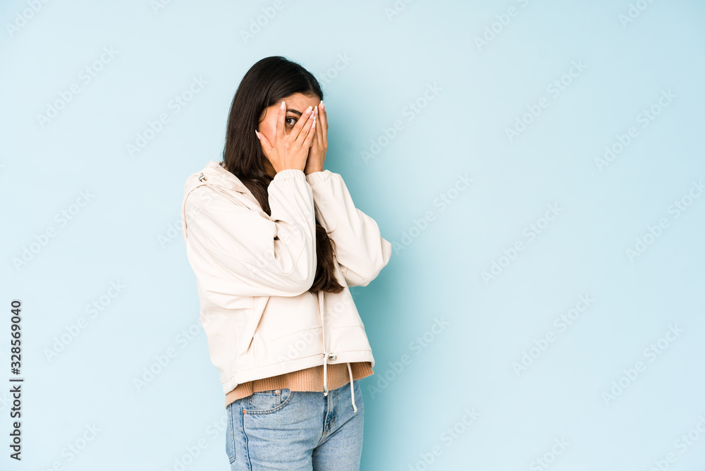 Young indian woman on blue background blink through fingers frightened and nervous. Young indian woman on blue background blink through fingers frightened and nervous.