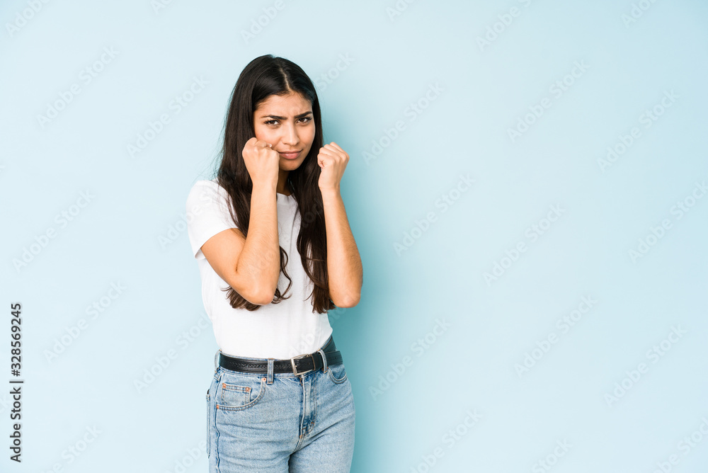 Young indian woman on blue background throwing a punch, anger, fighting due to an argument, boxing. Young indian woman on blue background throwing a punch, anger, fighting due to an argument, boxing.