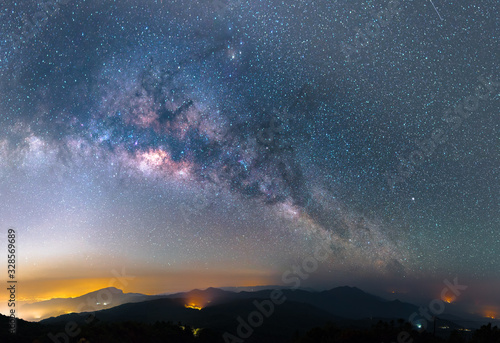 The Panorama of arching Milky Way galactic center over the mountain with city light.