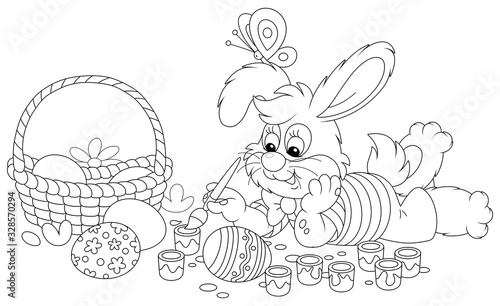 Happy little bunny painting beautiful Easter eggs with bright and colorful paints and an art paintbrush, black and white vector cartoon illustration for a coloring book