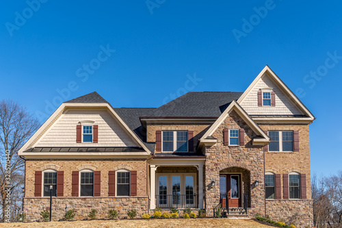 Front view of American luxury single family mansion with curb appeal with large double hung sash arch windows dark bar shutters, covered entrance way, gable and gambrel roof in Maryland