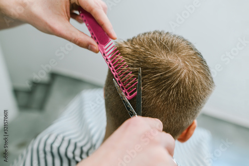 Hairdresser cuts hair of man with blond hair with scissors and comb, close photo of barber's hands. Creating stylish haircut in barber shop concept. Close photo. Background Copy space