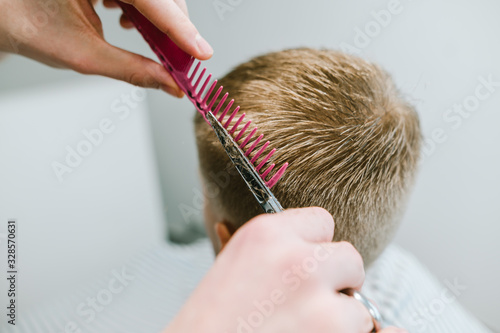 Closeup photo of a barber's hair clipping a blond client's hair with scissors and using a comb. Creating stylish male haircut concept. Copy space