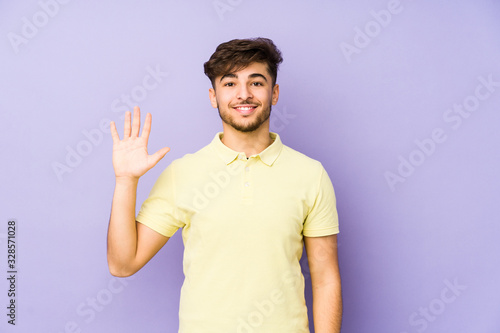 Young arabian man isolated on a purple background smiling cheerful showing number five with fingers.