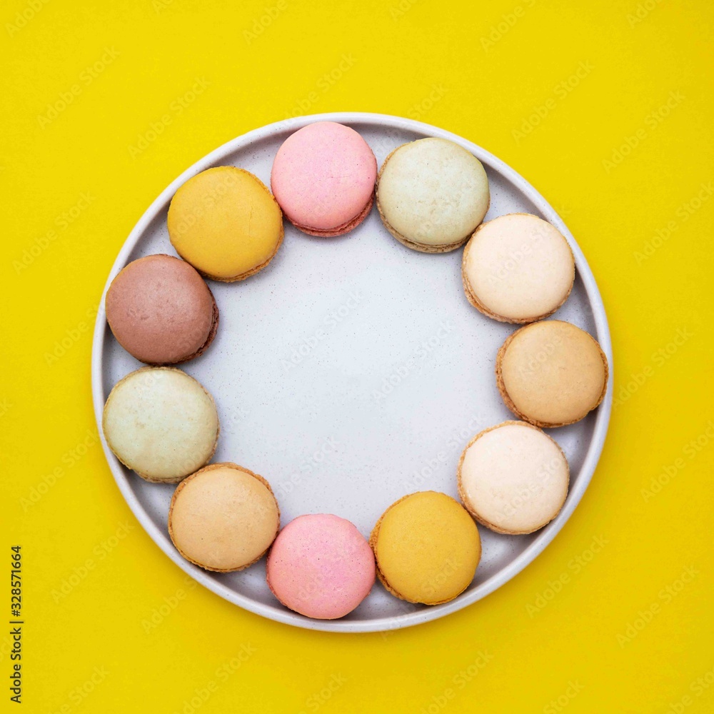 Colorful macaroons cookies dessert on a plate, with yellow background. Colorful macaroons cookies dessert on a plate, with yellow background.