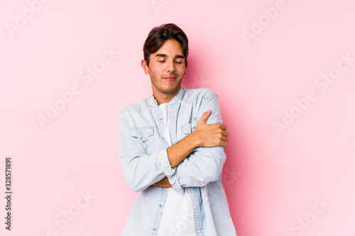 Young caucasian man posing in a pink background isolated hugs, smiling carefree and happy. © Asier