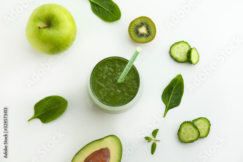 Freshly made green smoothie made of vegetables, fruits, herbs and greens. Glass of blended vegan beverage with ingredients around. Top view, close up, copy space, background.