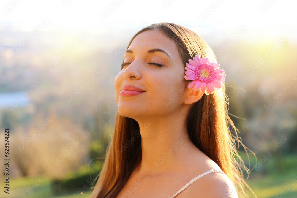 Close up portrait of beautiful relaxed girl with pink flower on ear breathing fresh air with closed eyes outdoor in spring time Close up portrait of beautiful relaxed girl with pink flower on ear breathing fresh air with closed eyes outdoor in spring time