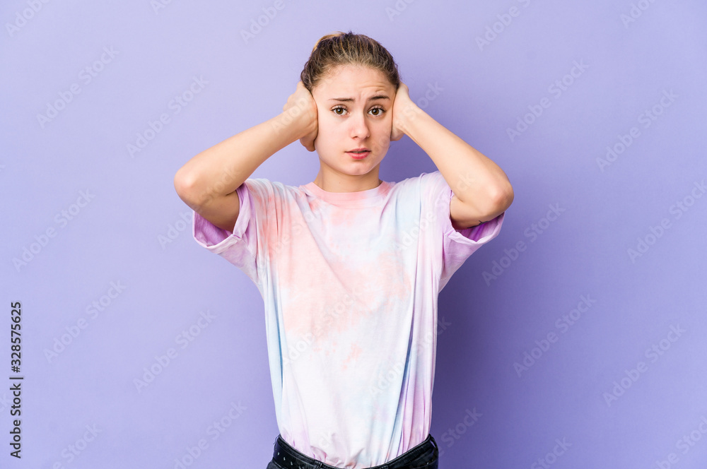 Young caucasian woman on purple background covering ears with hands trying not to hear too loud sound. Young caucasian woman on purple background covering ears with hands trying not to hear too loud sound.