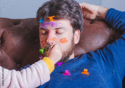 Father's day. Young man sleeping while his little daughter paints his face
