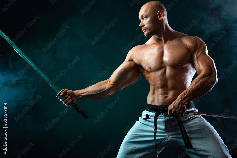 Karate fighter on black background with smoke. Shirtless man samurai with Japanese sword. Fit man sportsmen bodybuilder physique and athlete. Men's sport motivation.
