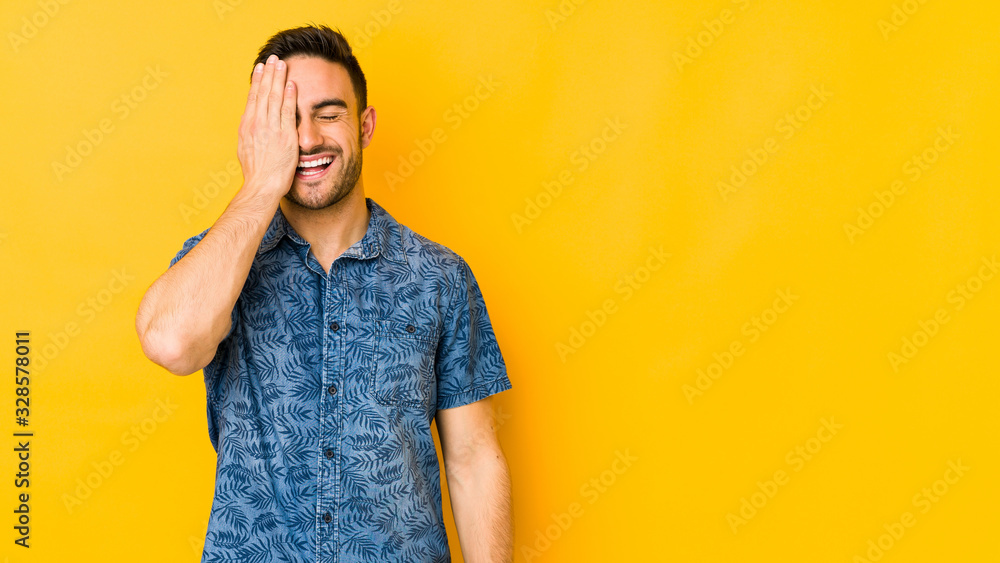 Young caucasian man isolated on yellow bakground having fun covering half of face with palm. Young caucasian man isolated on yellow bakground having fun covering half of face with palm.