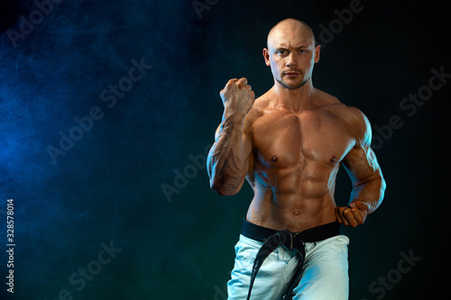 Karate or taekwondo fighter on black background with smoke. Fit man sportsmen bodybuilder physique and athlete. Men's sport motivation. © Mike Orlov