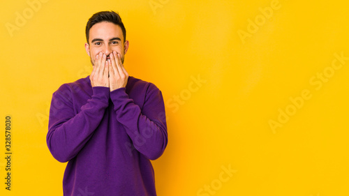 Young caucasian man isolated on yellow bakground laughing about something, covering mouth with hands.